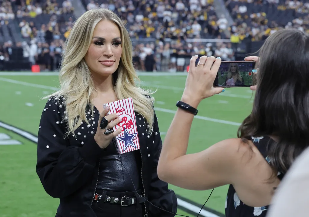 Recording artist Carrie Underwood films a promo on a football field, holding a 