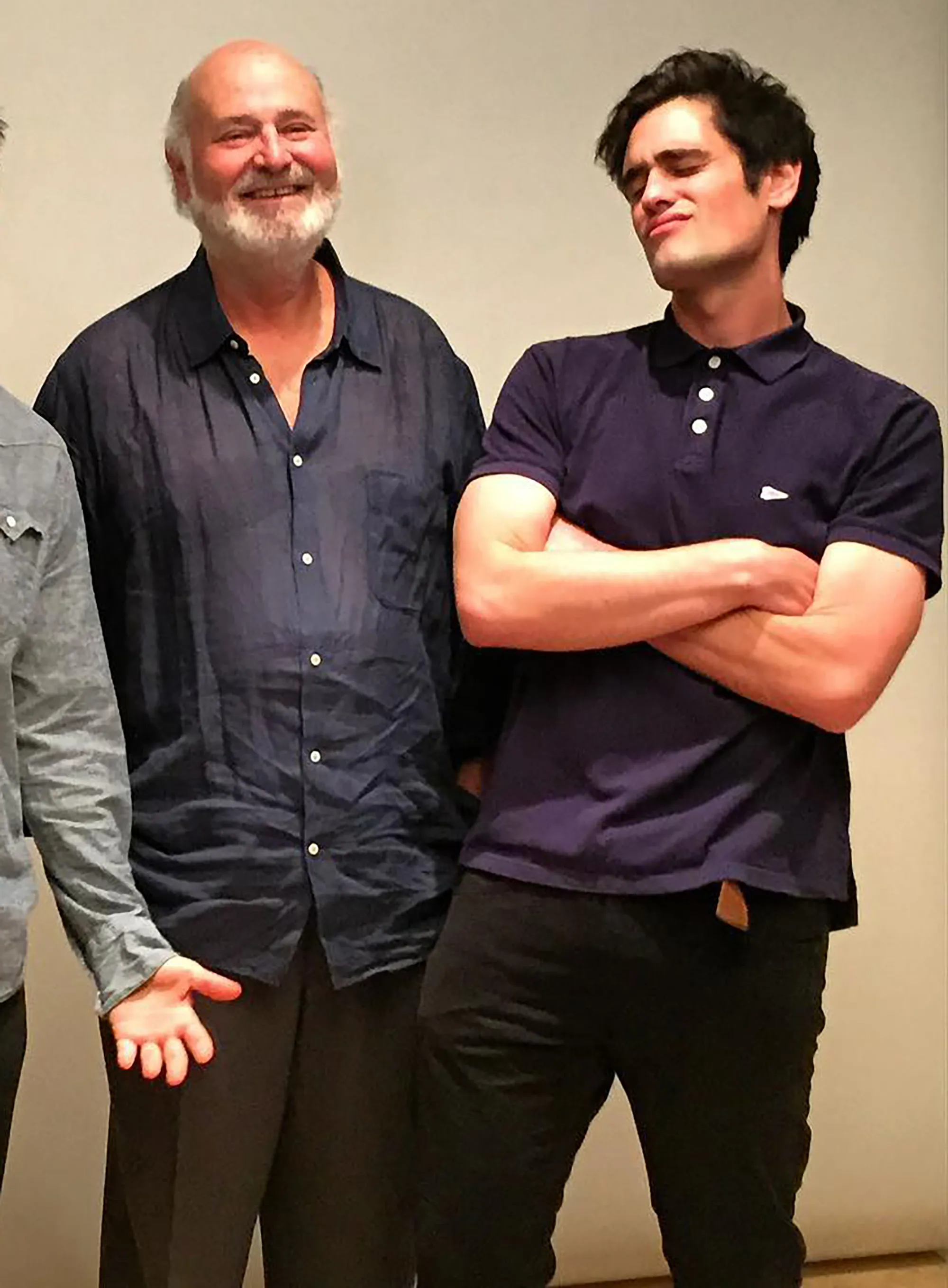 Rob Reiner and his son Nick stand side-by-side, Rob smiling at the camera and Nick looking upward with a smirk.