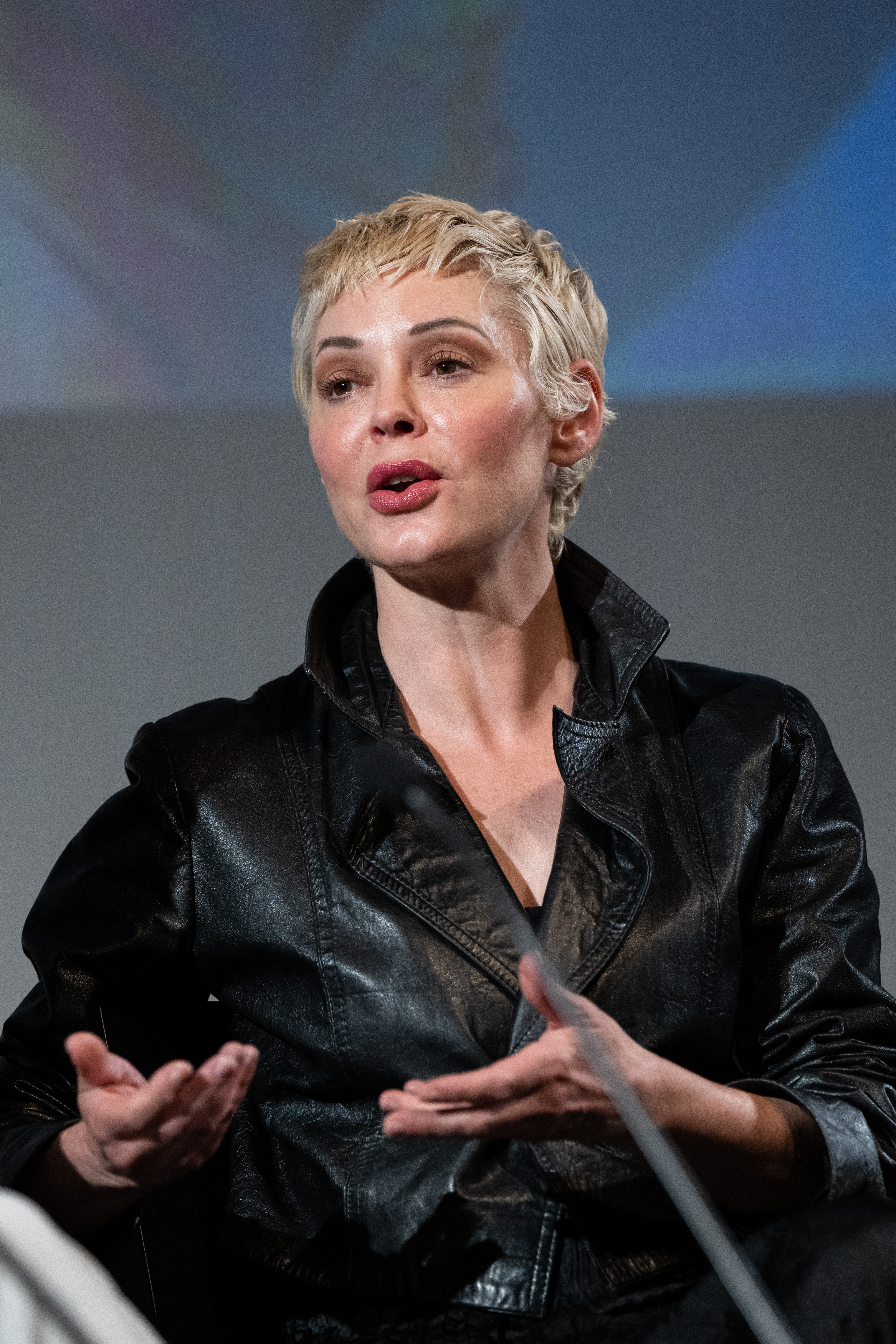 Rose McGowan speaking at an event, gesturing with her hands.