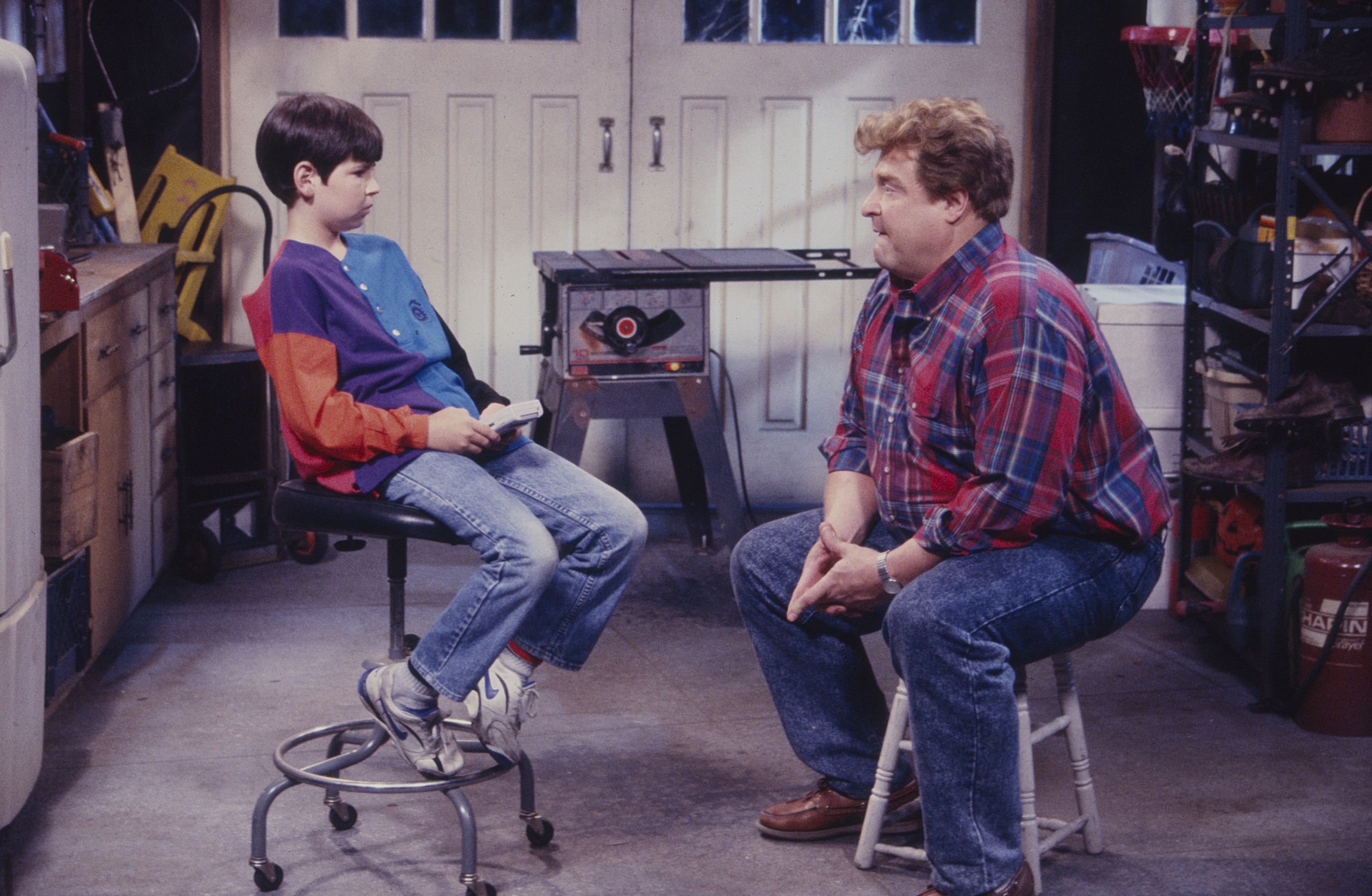 John Goodman and Michael Fishman seated in a garage, from 