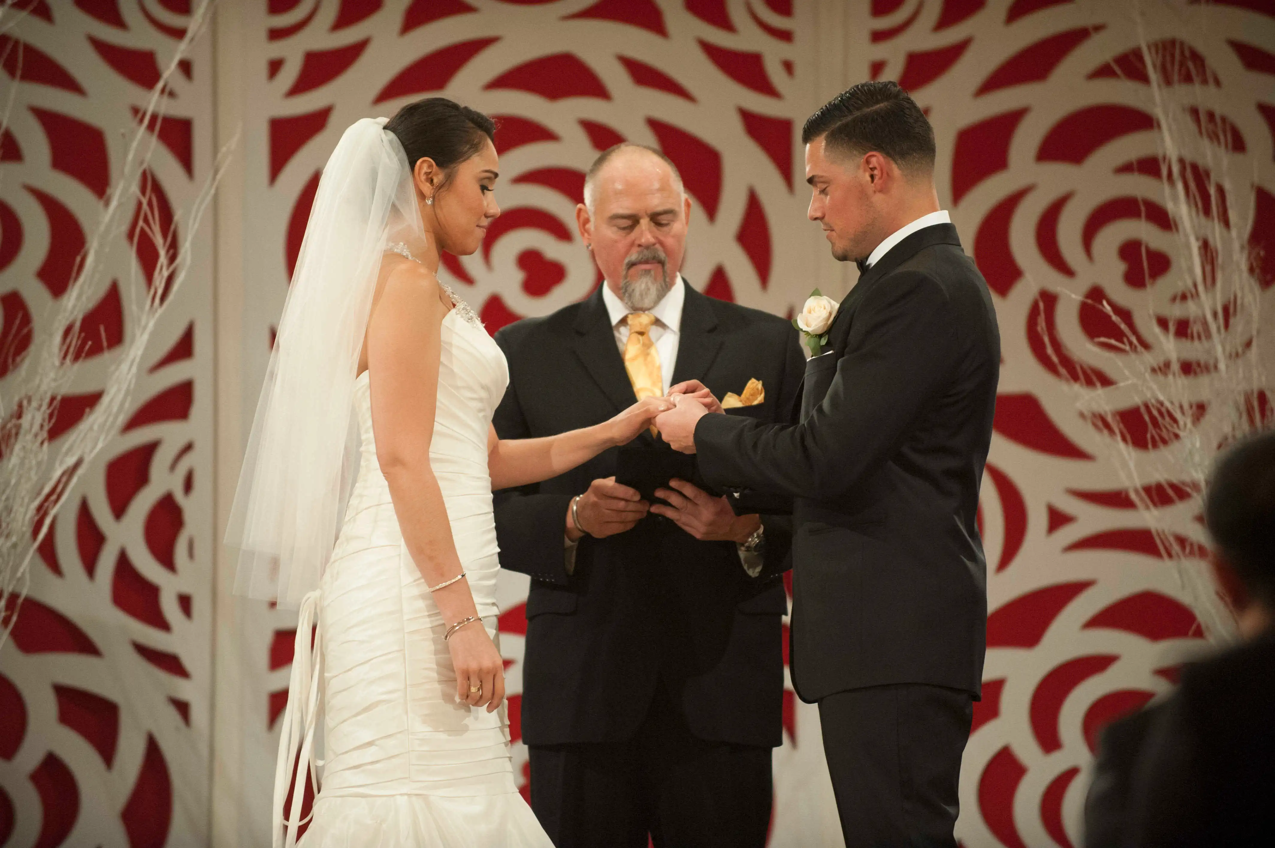 A man and woman exchanging rings during their wedding ceremony with an officiant looking on.