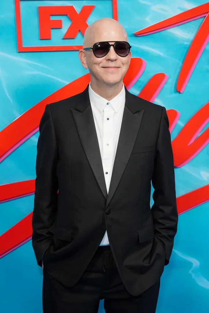 Ryan Murphy wearing sunglasses and a black tuxedo jacket with an open white shirt at