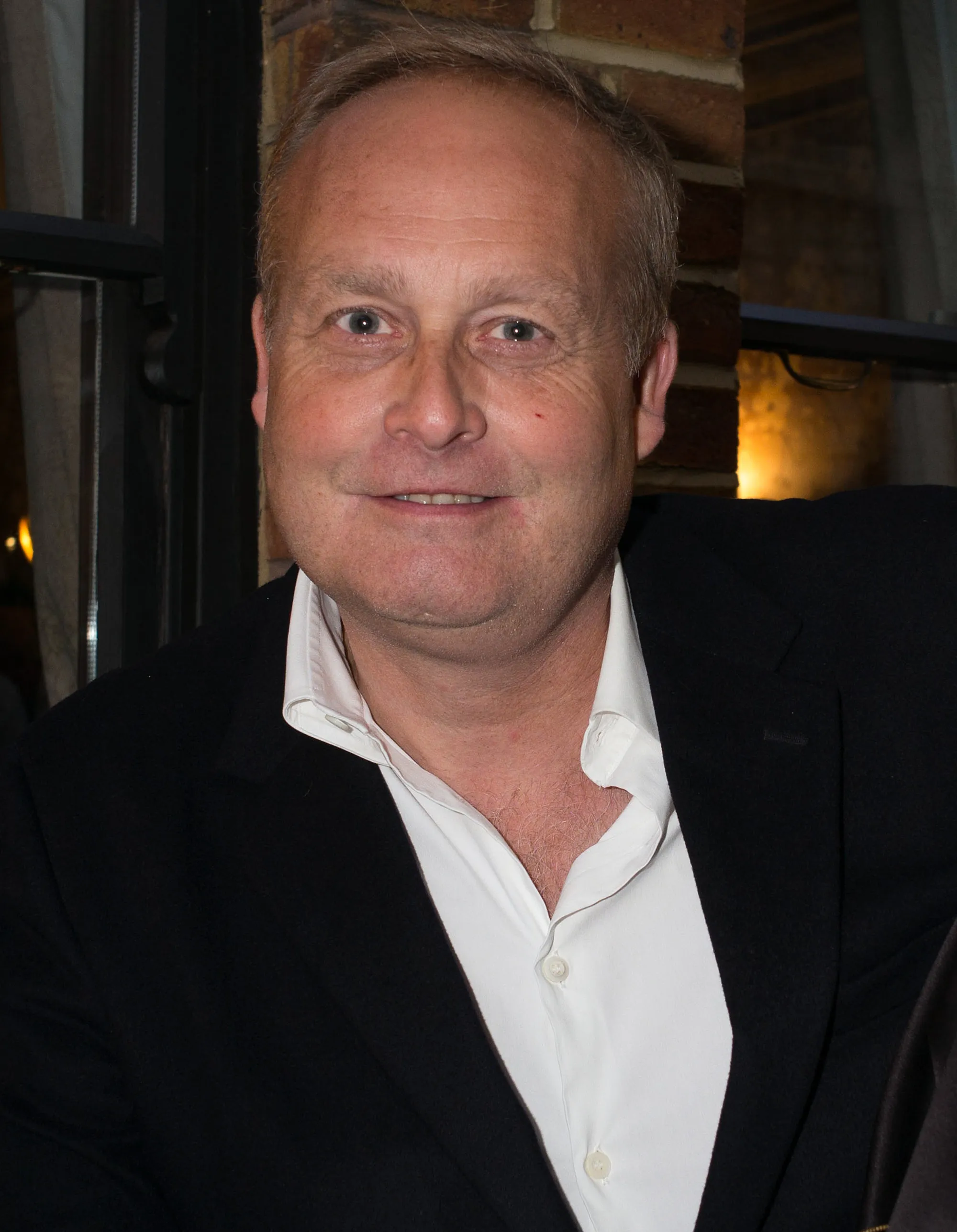 A smiling Ian Wace in a black suit jacket and white open-collared shirt.