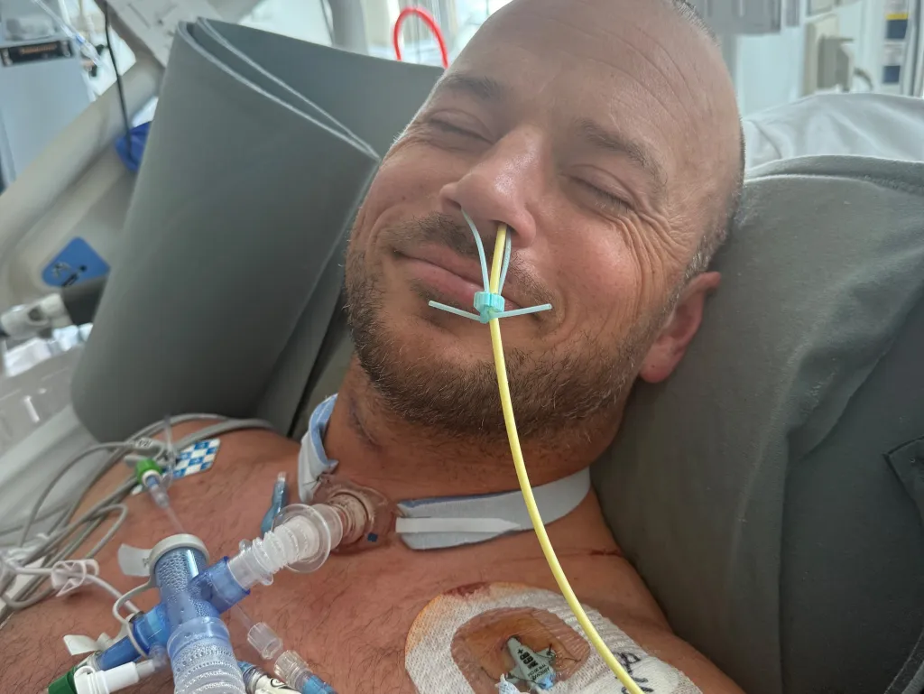 Josh Collette, a San Clemente father of five, is seen lying in a hospital bed with tubes in his nose and chest, having been paralyzed from the neck down after diving into the ocean to help a child caught in a rip current.