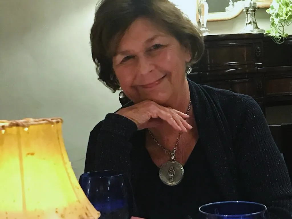 Nancy Guthrie smiling, wearing a dark sweater and a round pendant.