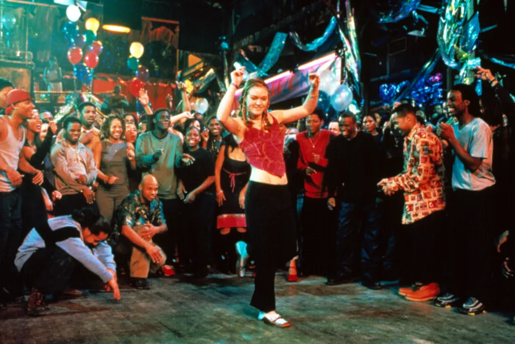 Julia Stiles dancing in a club, with onlookers cheering her on.
