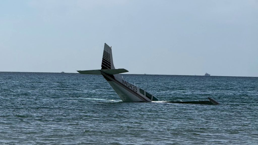 A small, single-engine plane, identified by its tail number N40439, partially submerged in the ocean off Boca Raton, Florida.