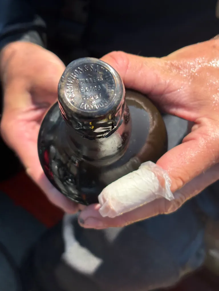 A person's hands holding a dark Guinness bottle with a tarnished metallic cap.