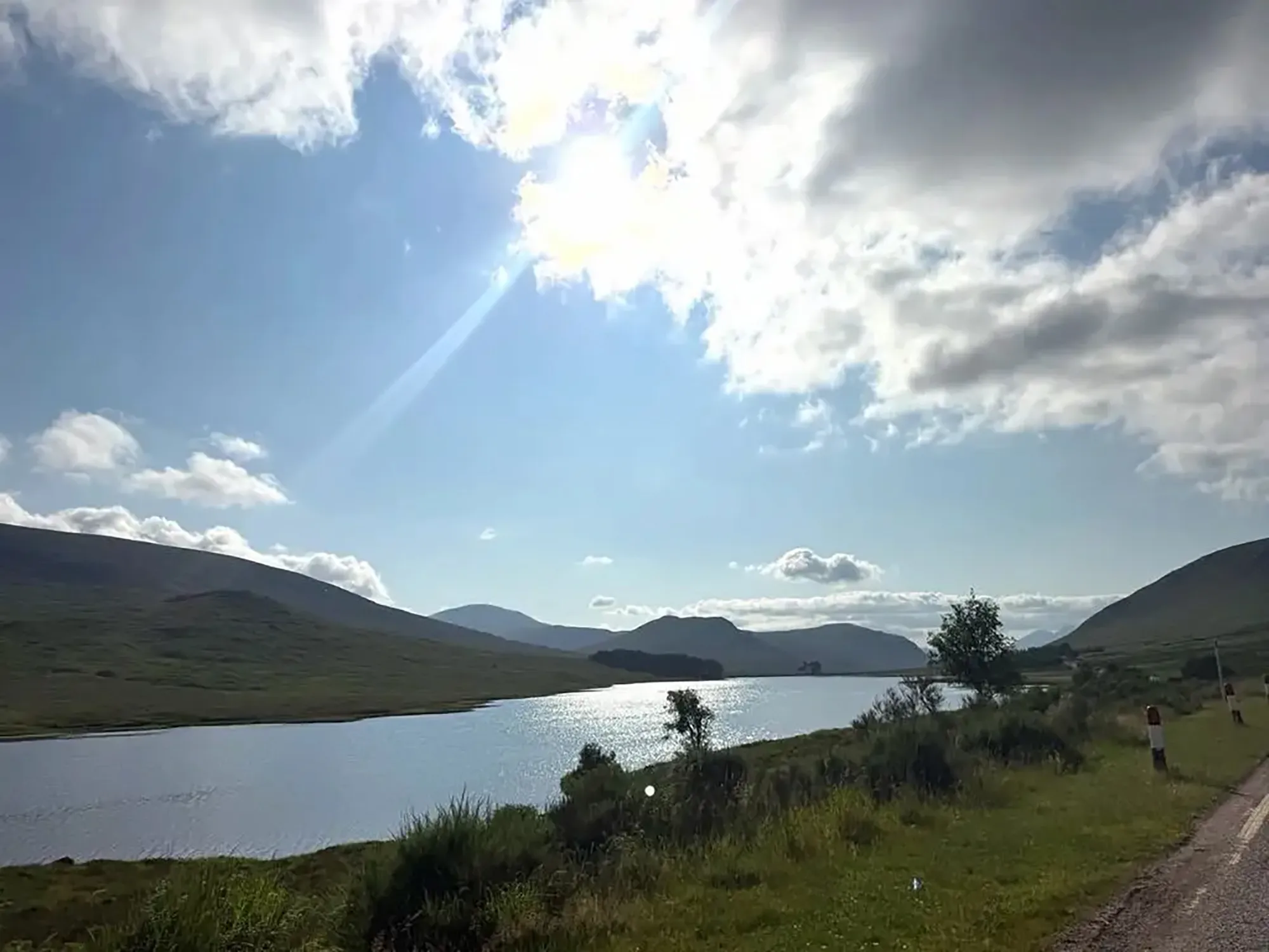 Scottish Highlands with a large lake and mountains under a bright sun.