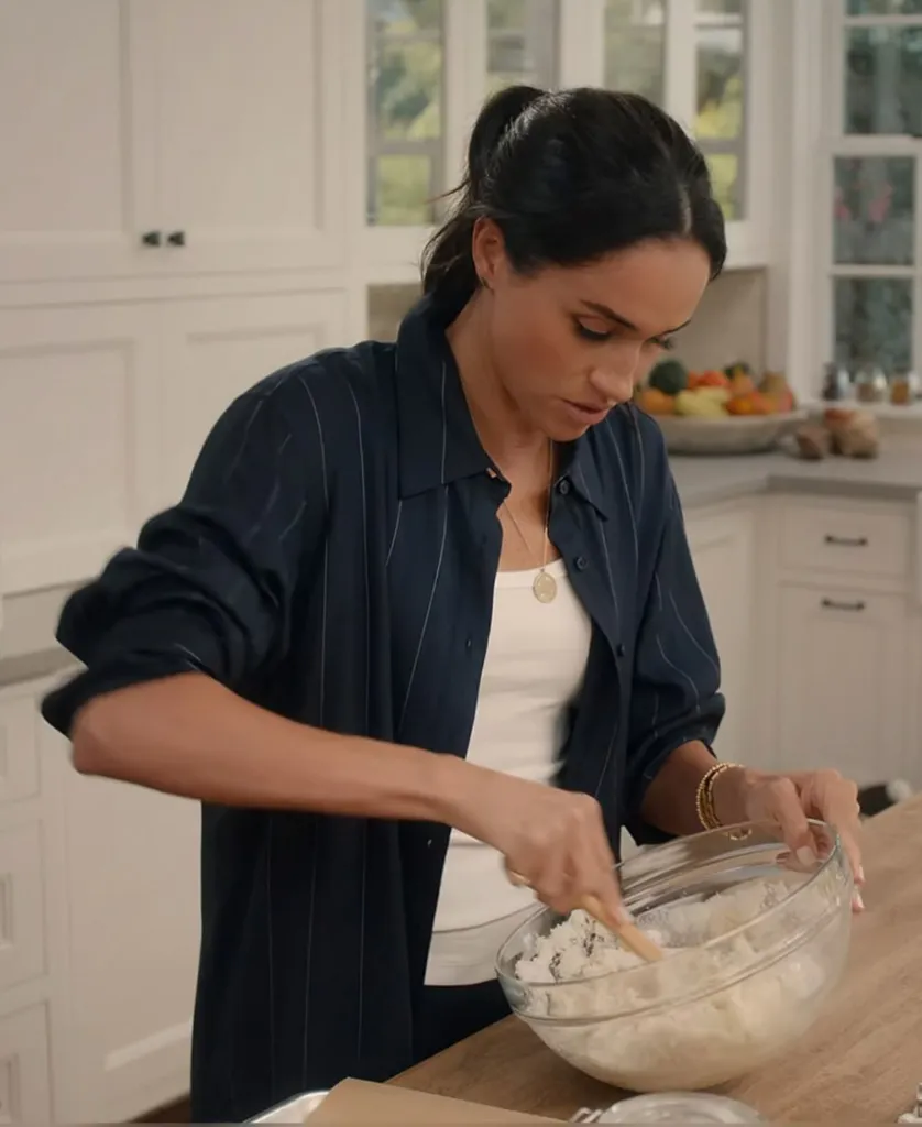 Meghan Markle mixing ingredients in a bowl while wearing signet stud earrings.