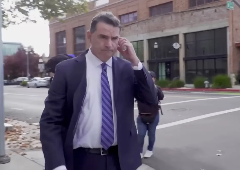Sean McCluskie, dressed in a suit and tie, walks outside.