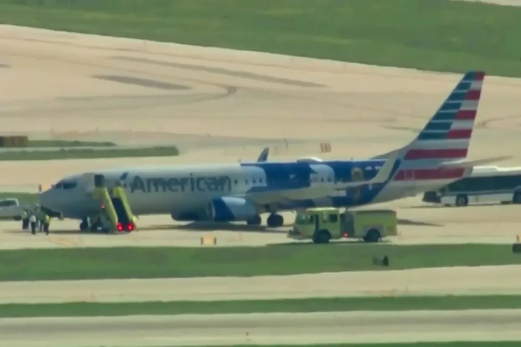 An American Airlines plane on the tarmac with a mobile stairway attached to its front door, with a yellow fire truck and bus nearby.