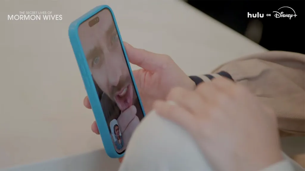 A woman holding a phone showing a video call with a man sticking out his tongue.