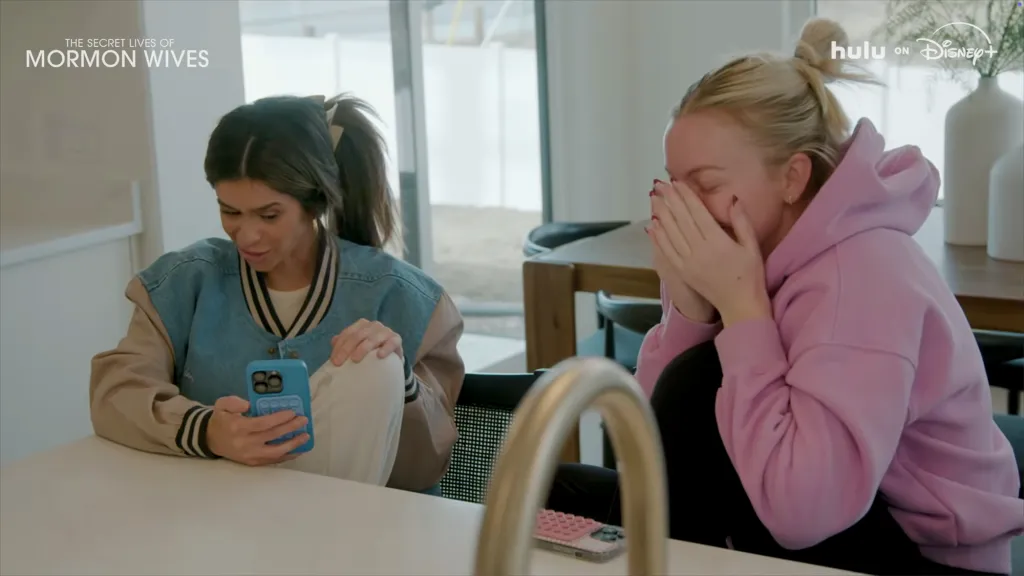 Two women, Taylor Frankie Paul in a bomber jacket looking at her phone, and another woman in a pink hoodie crying, from 