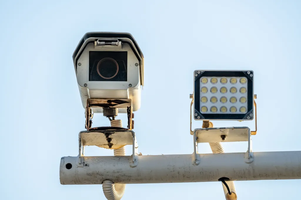 Security camera and flood light on a pole against a blue sky.