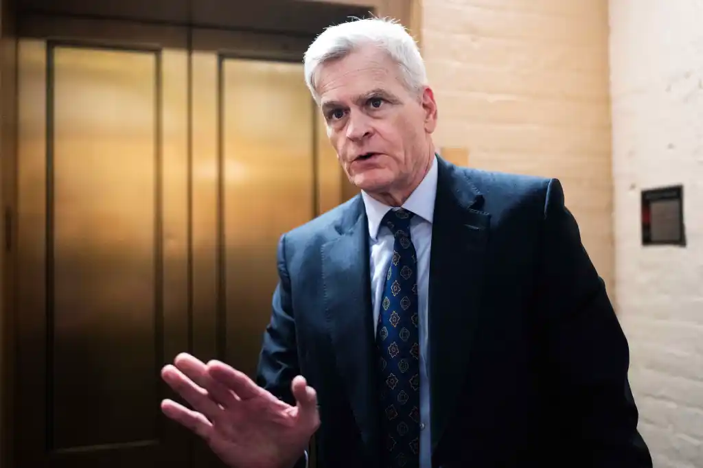 Senator Bill Cassidy speaks to reporters, gesturing with his right hand.