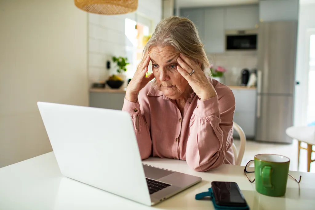 Senior woman feeling stressed while working on a laptop at home.
