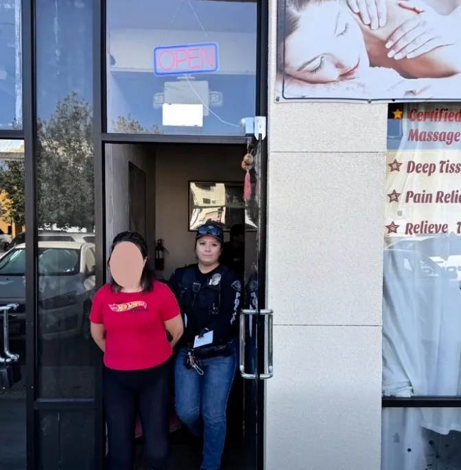 A police officer escorting a woman out of a massage parlor with an 