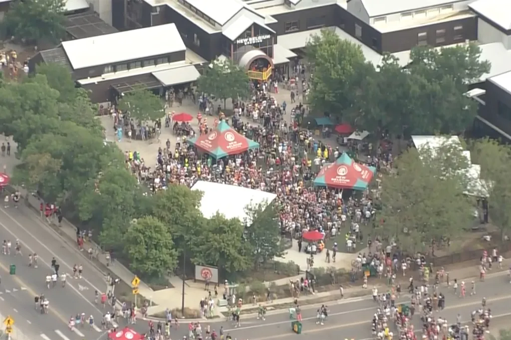 Aerial view of a large gathering of people outside New Belgium Brewing, with tents and people walking along a street in the foreground.