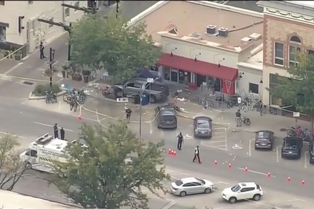 Overhead view of a street blocked off by police tape and officers, where a pickup truck has crashed onto a sidewalk, littering it with debris.