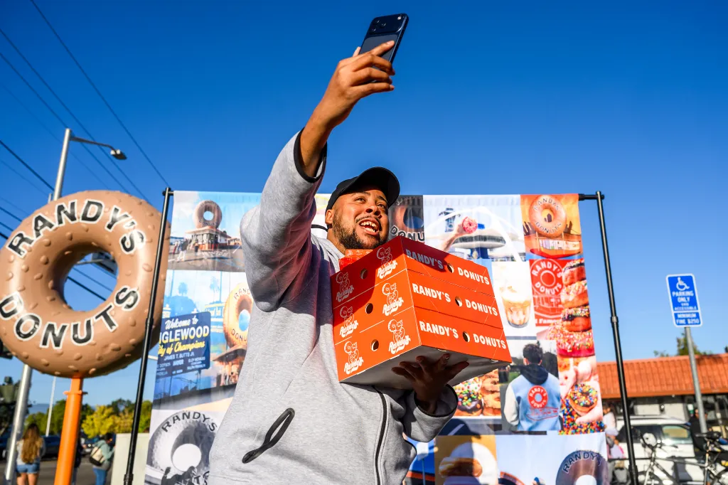 Shawn Lenelle takes a video with four boxes of Randy's Donuts in hand during the grand opening.