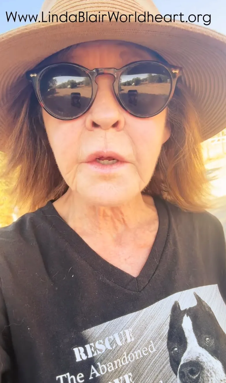 Linda Blair wearing a hat and sunglasses, with a black t-shirt featuring a dog and the words