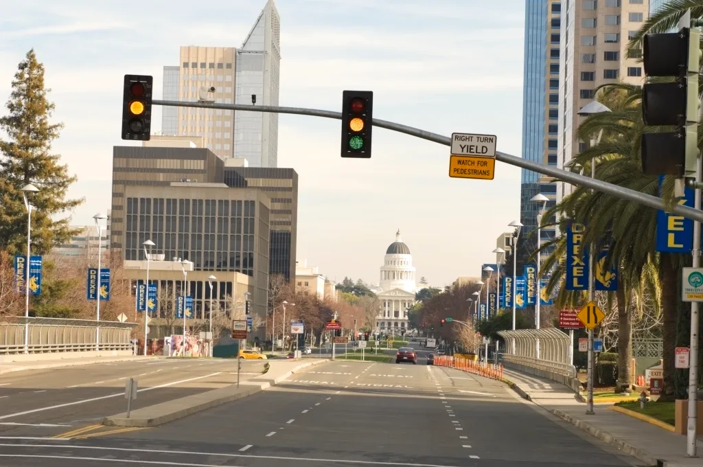 Road leading to the California State Capitol building, with tall buildings and palm trees lining the road.