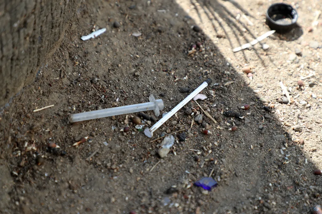 Drug paraphernalia, including a needle and plunger, on the ground.