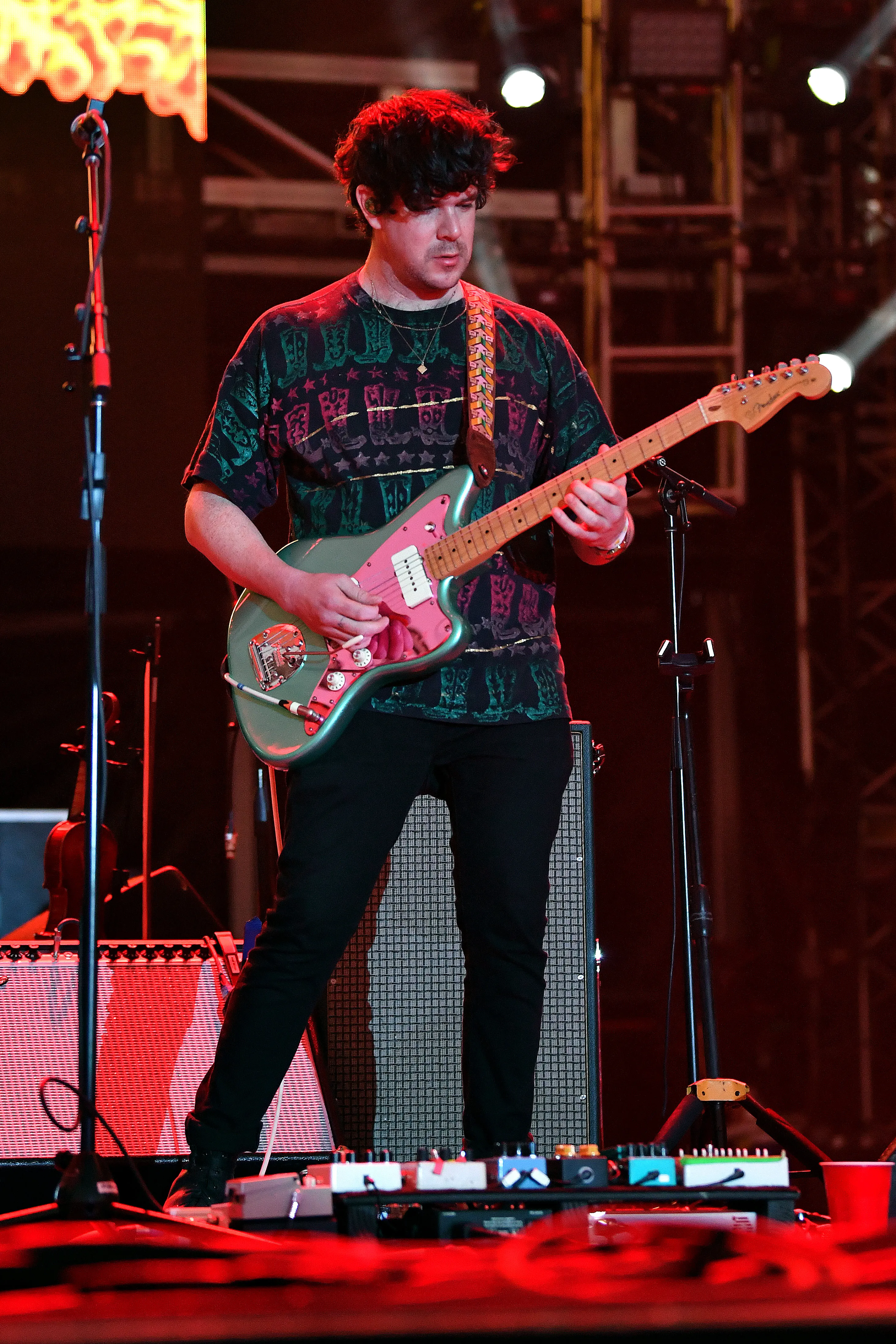 Simon O'Connor of Modest Mouse performs on stage, playing a green and pink electric guitar.