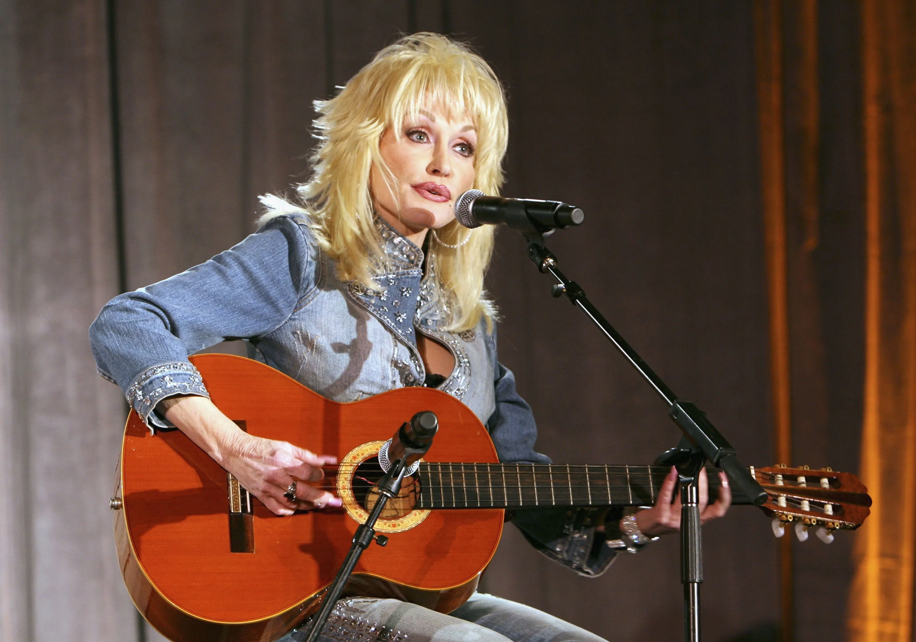 Dolly Parton performing on stage, playing a guitar and singing into a microphone.