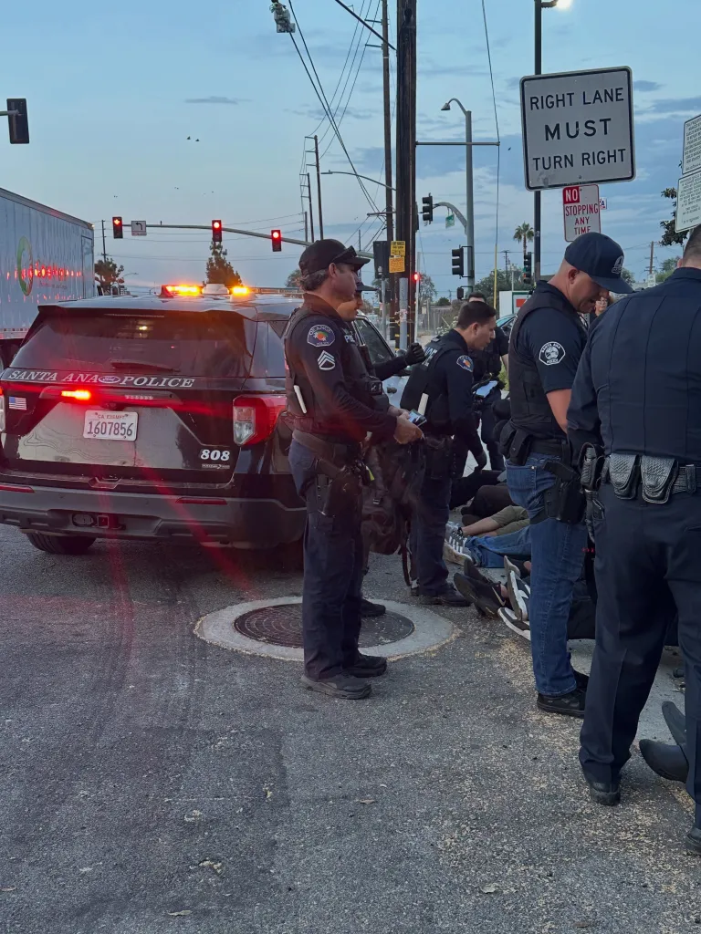 Police officers conducting a homeless sweep, with one police vehicle and individuals lying on the ground.