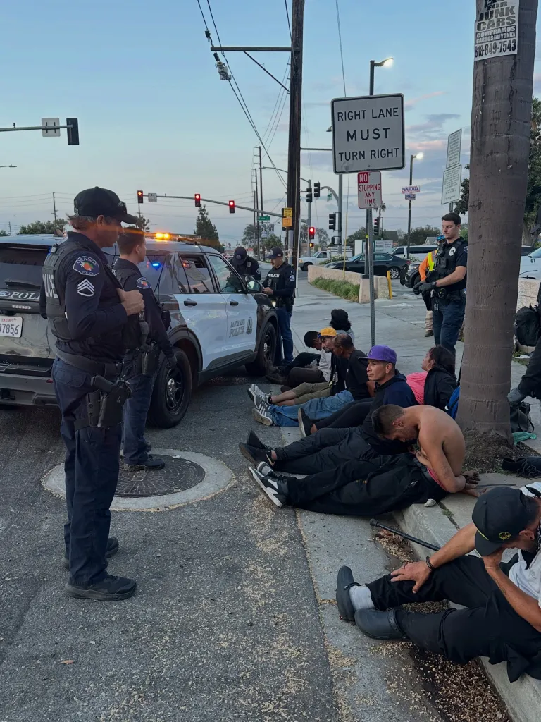 Police officers overseeing a group of people sitting on the curb of a street in Orange, California.