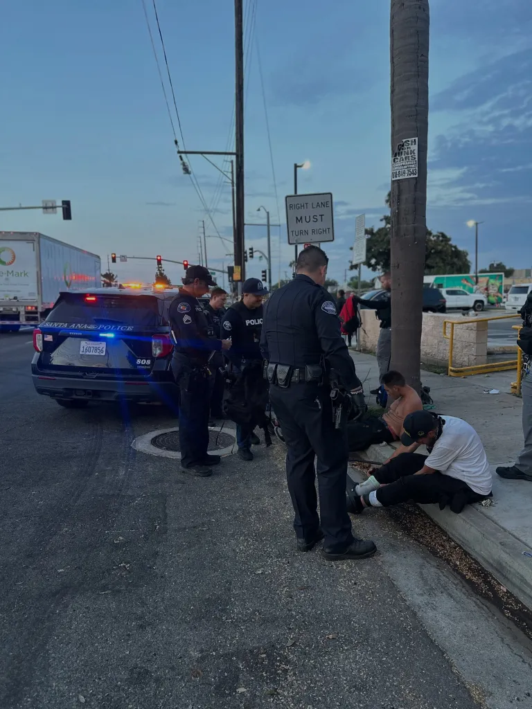 Police officers arresting two men sitting on a curb in Orange, California.