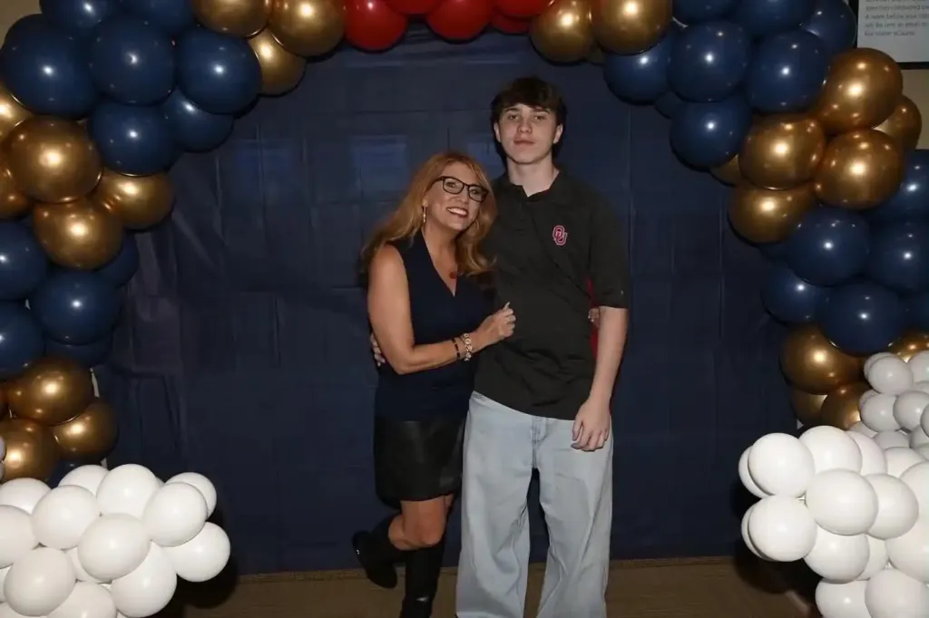 Jenny Lupton and her son standing in front of a blue backdrop adorned with a balloon arch.