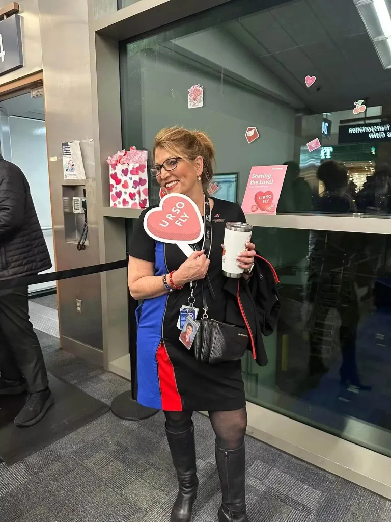 Jenny Lupton, a Southwest Airlines flight attendant, smiling and holding a heart-shaped sign that reads