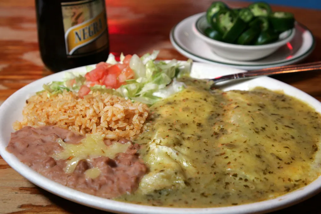A plate of spinach and cheese enchiladas with rice, refried beans, and salad.