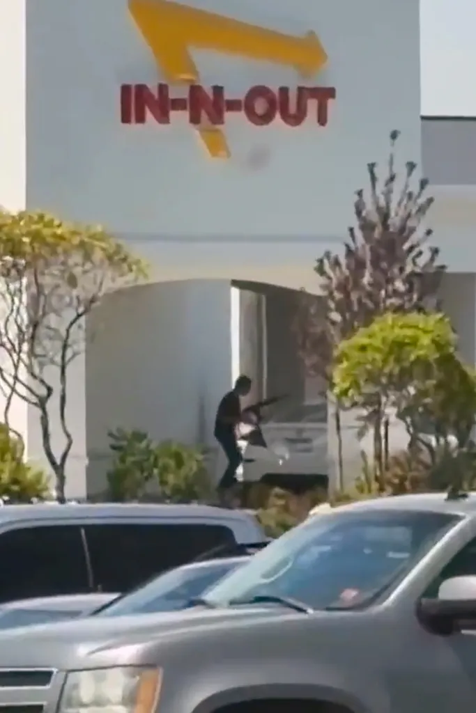 A still image from video shows a person with a gun in front of an In-N-Out Burger restaurant.