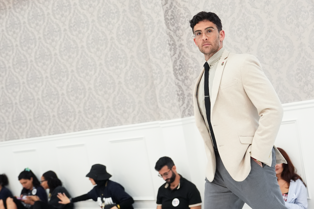 Hasan Piker, a streamer, in a cream blazer and glasses, looks toward the camera at a campaign event.