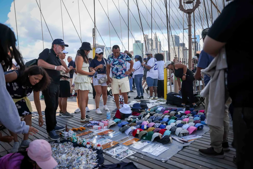 People browse souvenirs, including hats and replica license plates, from street vendors on the Brooklyn Bridge walkway.