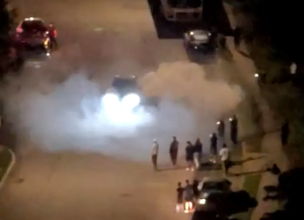 Car emitting smoke from its tires with a crowd watching during a street takeover event.