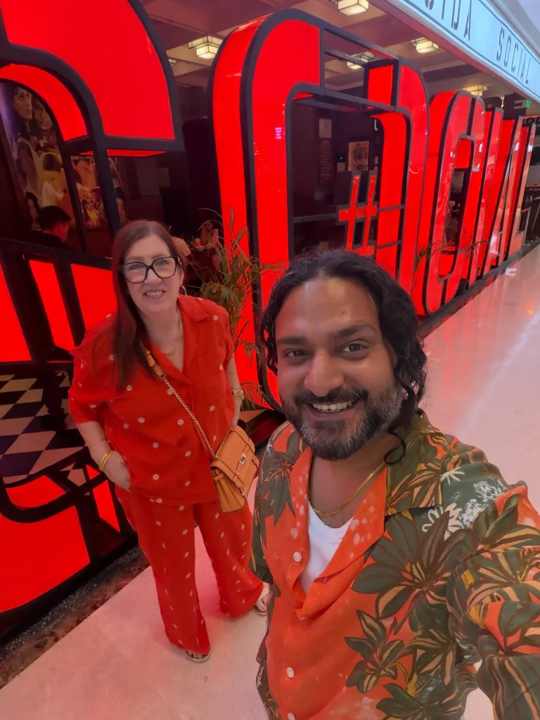 Sumit and Jenny from 90 Day Fiancé smiling in front of a red sign.