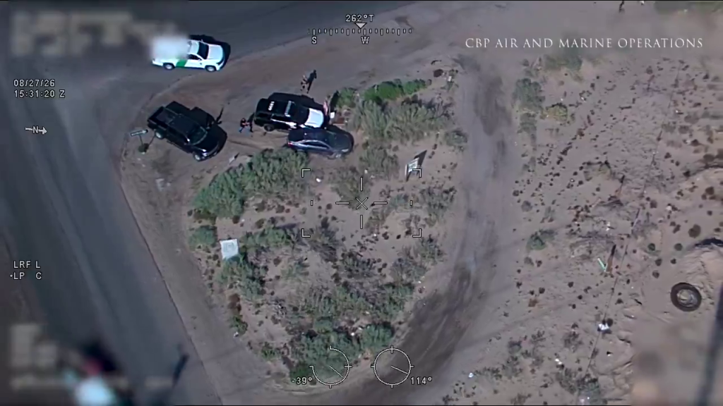 Aerial view from a CBP aircraft showing three vehicles and several individuals in a desert area.