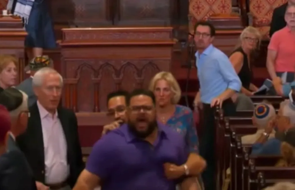 Man in purple shirt being escorted out of a synagogue.