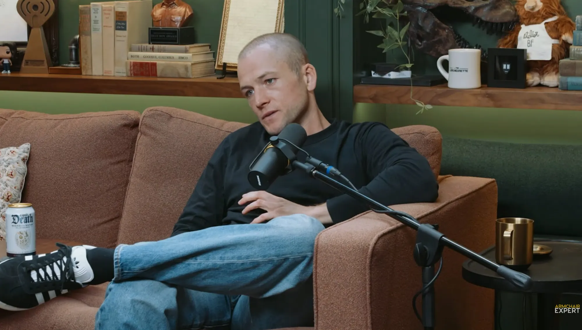 Taron Egerton sitting on a couch with a microphone in front of him.