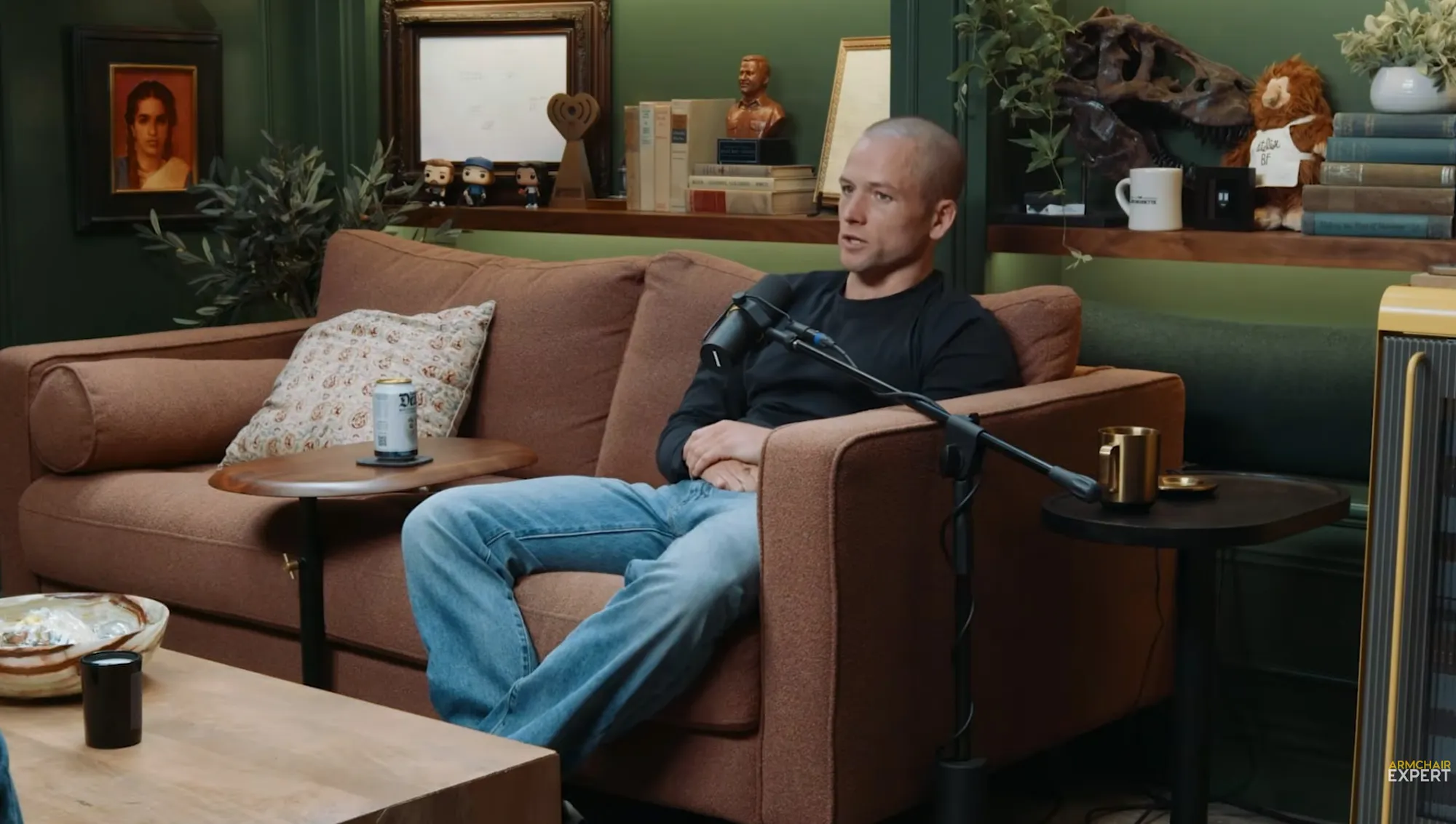 Taron Egerton sitting on a couch with a microphone in front of him.