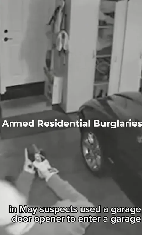 Black and white security camera footage showing a person on the ground holding a gun, a car, and an open cabinet inside a garage, with the text 