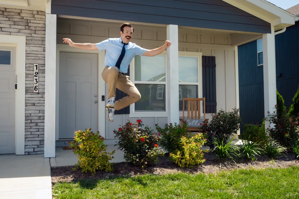Ted Lasso jumping on the porch of a home.