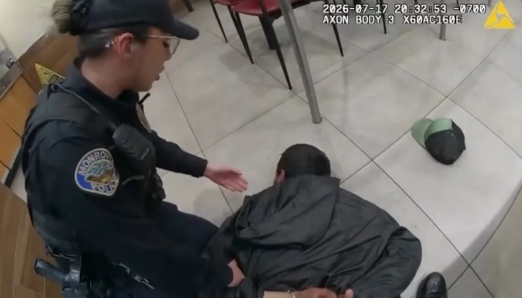 A female Monrovia Police officer kneeling next to a suspect, who is on the ground with his hands cuffed behind him.