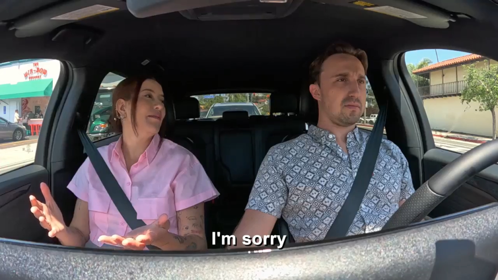 A man and a woman in a car, with the woman saying