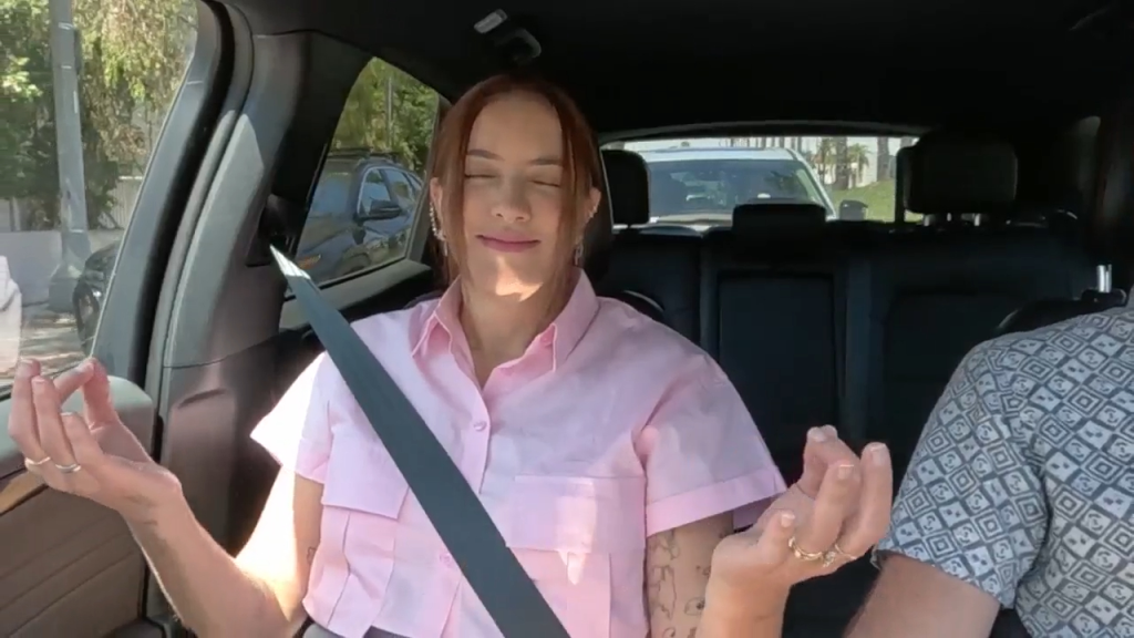A woman in a pink shirt practices meditation in a car.